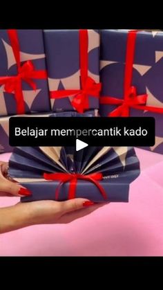 a hand holding a stack of gift wrapped in purple and red ribbon with the words beljaar meme percantik kado