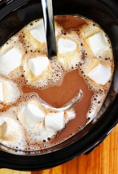 a cup of hot chocolate and marshmallows in a crock pot with a spoon