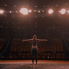 a woman is standing in front of an empty stage with her arms outstretched and hands out