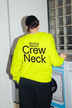 a woman wearing a neon yellow crew neck sweatshirt standing in front of a washing machine