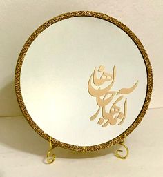 a white plate with gold glittered writing in the middle and an arabic calligraphy on it