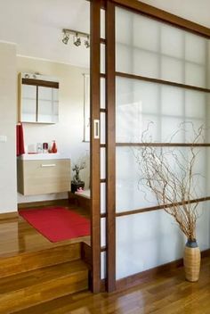 an open door leading to a bathroom with wood flooring and white walls, along with a red rug