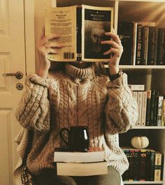 a person sitting in a chair holding up a book and coffee mug to their face