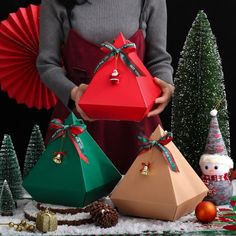 a woman holding three presents in front of christmas trees and decorations with red paper fans