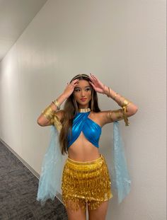 a woman in a blue top and gold skirt posing for the camera with her hands on her head