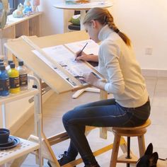 a woman sitting at a desk writing on a piece of paper next to a dog