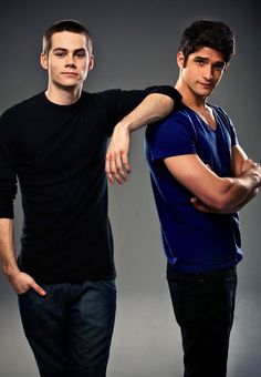 two young men standing next to each other in front of a gray background with one holding his arm around the other's shoulder