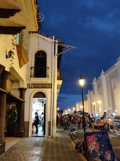 people are walking down the street in front of some buildings at night with lights on