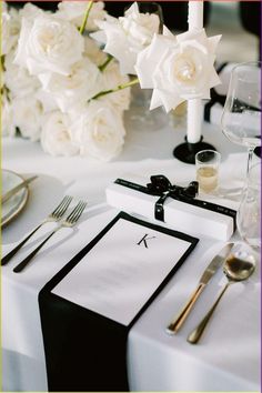 the table is set with white flowers and silverware for an elegant wedding reception in black and white