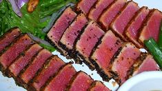 slices of meat and greens on a plate with dipping sauce in a bowl next to it