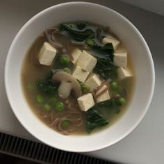 a bowl of soup with tofu, peas and spinach in it on a table