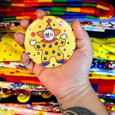 a hand holding a yellow button with a clown on it in front of colorful fabrics