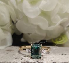 an emerald colored ring sitting on top of a rock next to white flowers and peonies