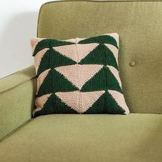 a green couch with a knitted pillow sitting on it's back and arm