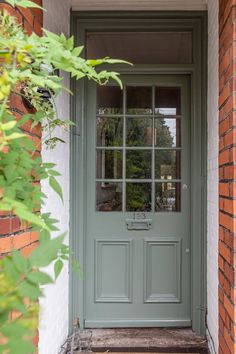 a green front door with glass panes on the side and brick building behind it