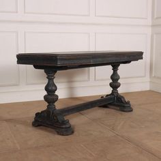 an old wooden table sitting on top of a tile floor next to a white wall