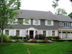 a house with white shutters and flowers in the front yard