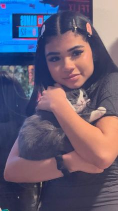 a woman holding a cat in her arms while standing next to a tv screen and smiling at the camera