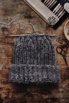 a knitted hat sits next to scissors and other crafting supplies on a wooden table