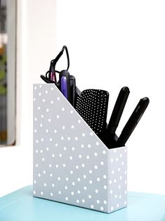 a polka dot pen holder holds pens, scissors and eyeglasses on a blue table