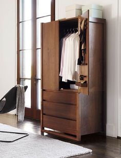 an open wooden wardrobe with clothes hanging on hangers and a chair in the foreground