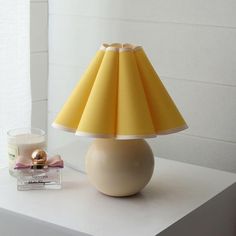 a yellow lamp sitting on top of a white table next to a glass candle holder