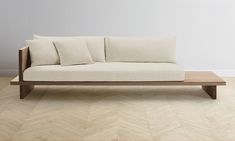 a white couch sitting on top of a wooden floor next to a wall with two pillows