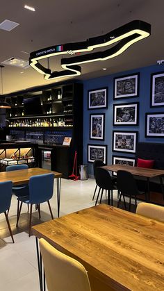 an empty restaurant with wooden tables and blue chairs, pictures on the wall behind them