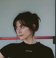 a woman with black hair wearing a black t - shirt and looking off to the side