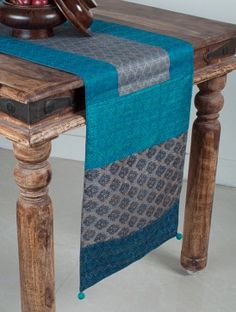 a wooden table topped with a blue and gray runner next to a bowl of fruit