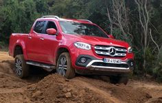 a red mercedes benz pickup truck driving through the mud on a dirt road with trees in the background