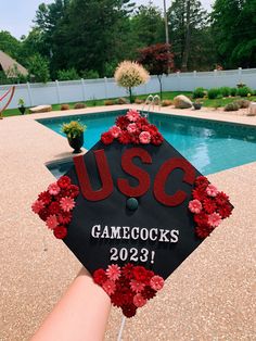 a graduation cap with flowers on it is held in front of a swimming pool that reads, u s c gamecocks