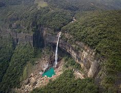 an aerial view of a waterfall in the middle of a forest with a lake below