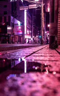 a city street at night with lights reflecting in the puddles on the pavement and buildings