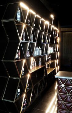 the shelves have bottles on them and lights are lit up in the dark behind them