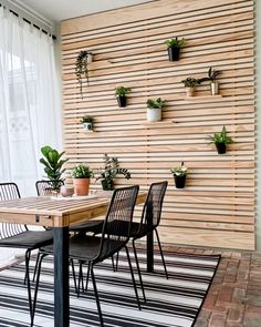 a dining room table with chairs and plants on the wall behind it, along with a striped rug