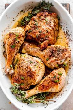 a white bowl filled with cooked chicken and garnished with herbs on the side