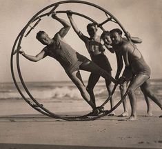 three men are doing tricks in a hoop on the beach while another man is standing behind them