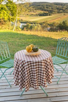 an outdoor table with two chairs and a checkered tablecloth on it in front of a grassy field