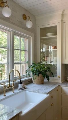 a white kitchen with marble counter tops and gold faucet lighting over the sink