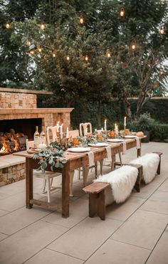 a woman standing in front of a table with candles and plates on it next to a fire place