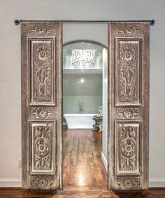 an open door leading to a bathroom with a tub and chandelier in the background