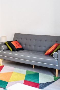 a grey couch sitting on top of a colorful rug in front of a white wall