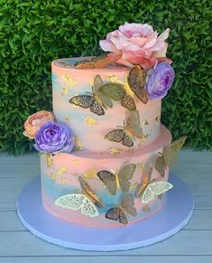 a three tiered cake with butterflies and flowers on the top, sitting on a blue plate