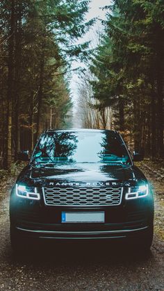 a black car parked on the side of a road in front of some tall trees