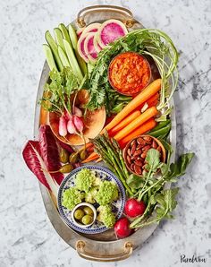 a platter filled with assorted vegetables on top of a white marble countertop