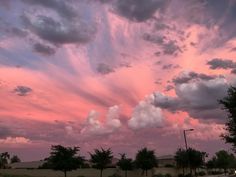 the sky is pink and purple as it sets in front of some trees with clouds