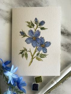 some blue flowers are sitting on top of a white paper and watercolor pencils