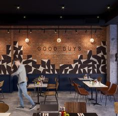 a man walking past a restaurant with tables and chairs in front of a brick wall