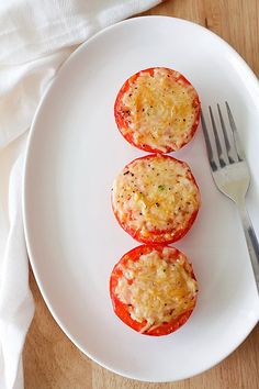 three stuffed tomatoes on a white plate with a fork